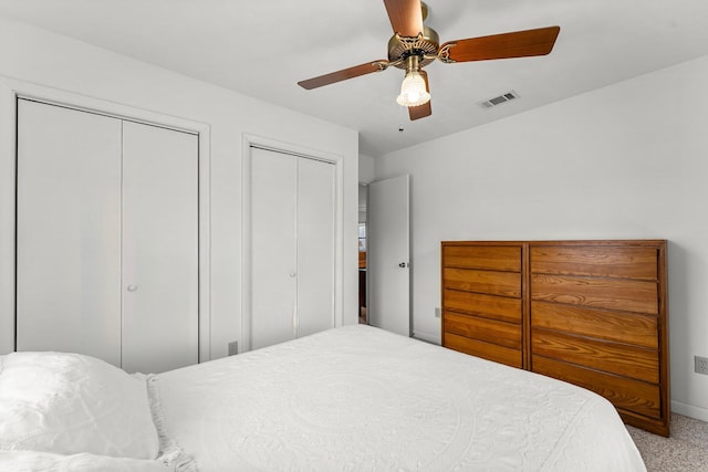 carpeted bedroom with multiple closets, visible vents, and a ceiling fan