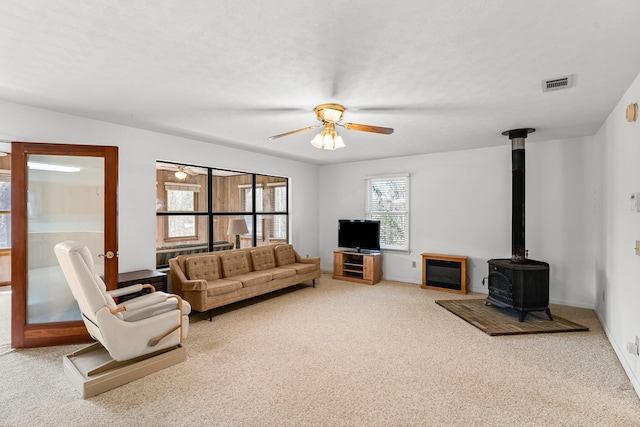 living area with a textured ceiling, visible vents, a ceiling fan, carpet, and a wood stove