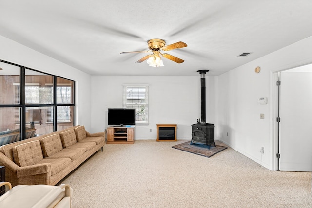 living area featuring baseboards, visible vents, a ceiling fan, a wood stove, and carpet floors