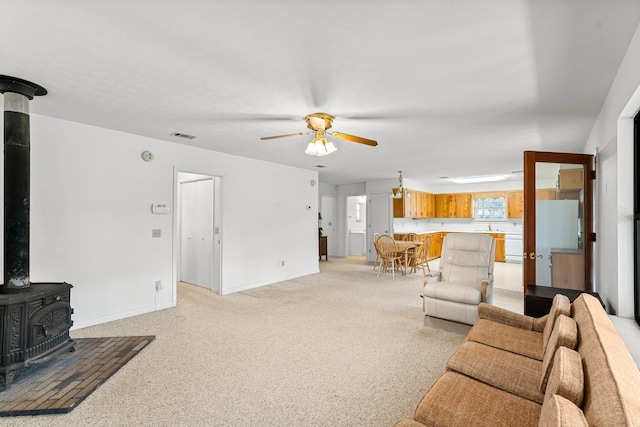 living room featuring baseboards, a ceiling fan, a wood stove, and light colored carpet