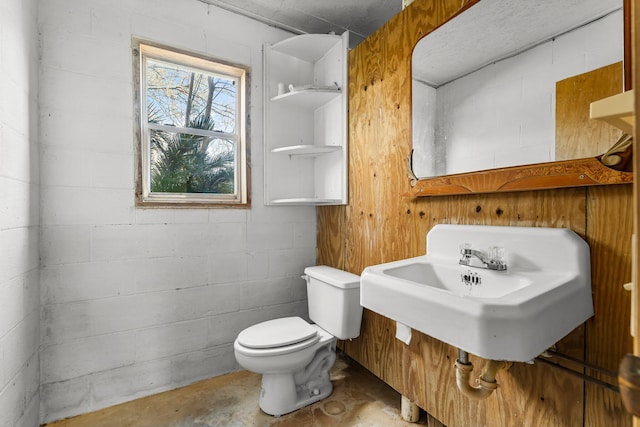 half bathroom with concrete block wall, a sink, toilet, and unfinished concrete floors