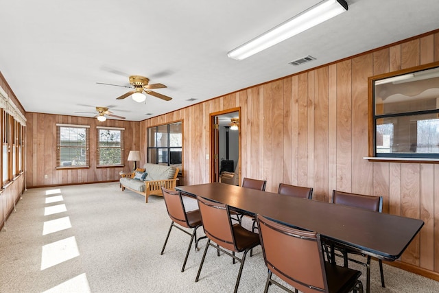 dining space with wood walls, visible vents, baseboards, a wood stove, and crown molding