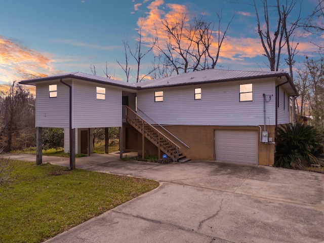 beach home with metal roof, a garage, stairs, concrete driveway, and a lawn