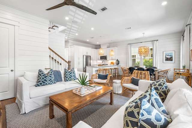 living room featuring wood walls, wood finished floors, visible vents, and a ceiling fan