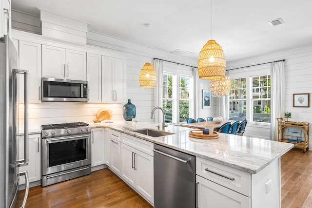 kitchen with dark wood-style floors, stainless steel appliances, white cabinets, a sink, and a peninsula