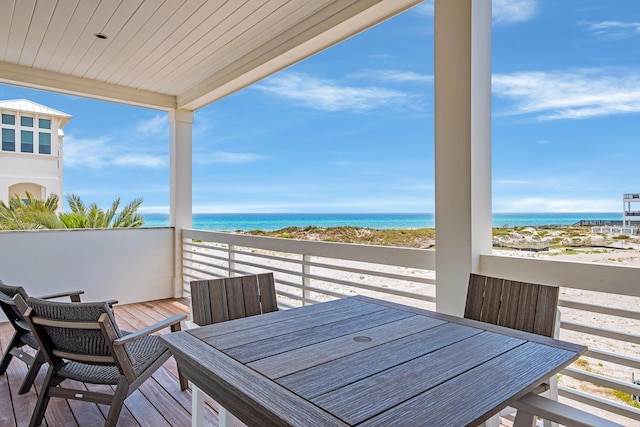 wooden terrace featuring a water view, a view of the beach, and outdoor dining space