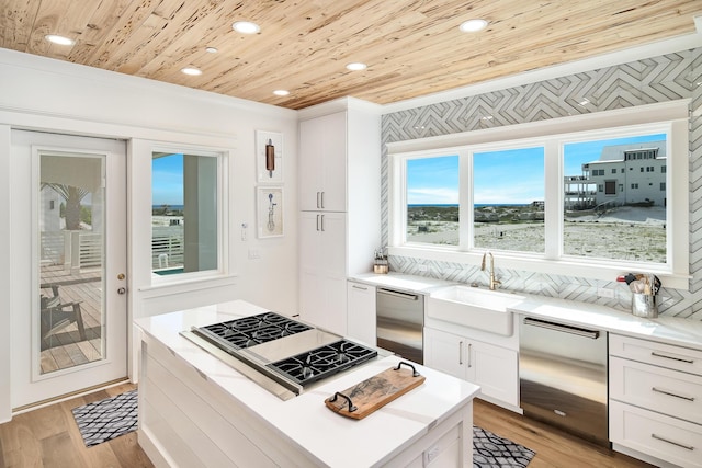 kitchen featuring a center island, stainless steel gas cooktop, light wood finished floors, wood ceiling, and a sink