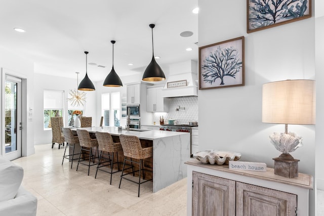 kitchen with a breakfast bar area, stainless steel appliances, light countertops, tasteful backsplash, and custom range hood