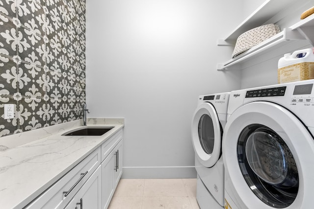 washroom featuring light tile patterned floors, cabinet space, baseboards, washing machine and clothes dryer, and a sink