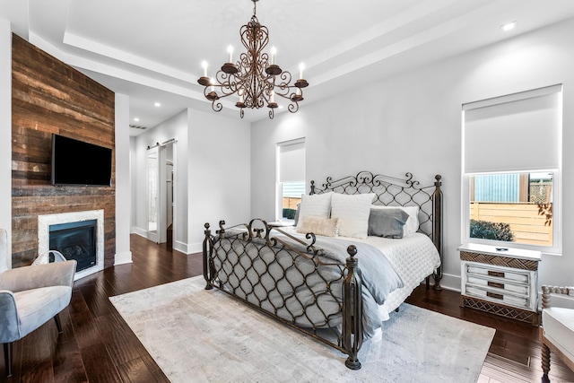 bedroom with a tray ceiling, a large fireplace, hardwood / wood-style floors, and a barn door