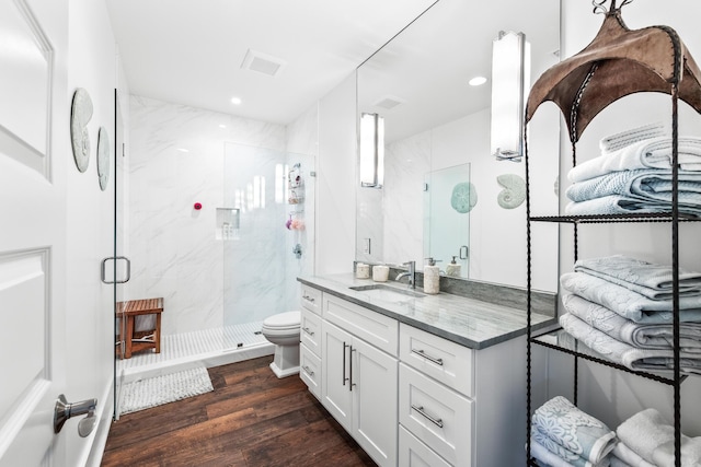 full bath with a marble finish shower, visible vents, toilet, vanity, and wood finished floors