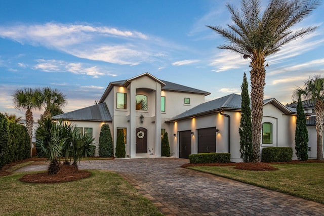 contemporary home featuring metal roof, decorative driveway, an attached garage, and stucco siding