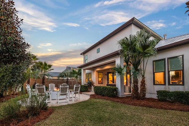 back of property at dusk with a patio area, fence, a lawn, and stucco siding