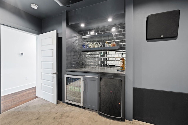 bar with light wood-style flooring, beverage cooler, baseboards, backsplash, and indoor wet bar