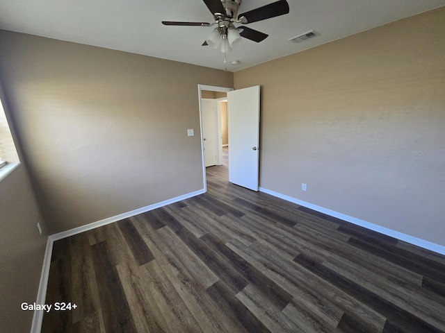 spare room with dark wood-type flooring, visible vents, ceiling fan, and baseboards