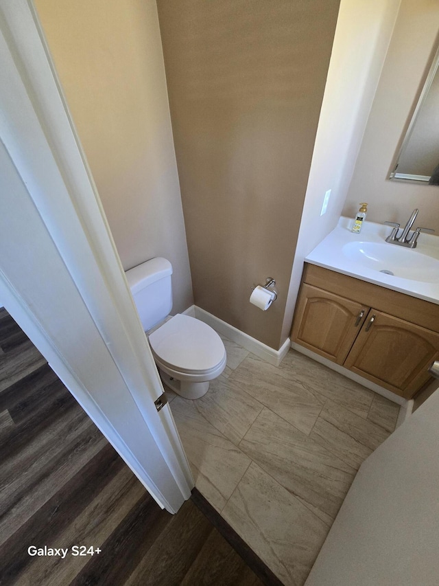 half bath featuring vanity, toilet, and baseboards