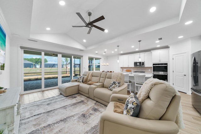 living area with recessed lighting, light wood-style flooring, a ceiling fan, lofted ceiling, and a tray ceiling