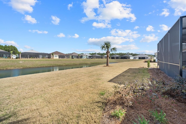 view of yard with glass enclosure, a residential view, and a water view