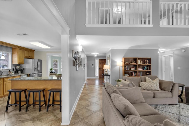 living area with light tile patterned floors, visible vents, a towering ceiling, ornamental molding, and baseboards