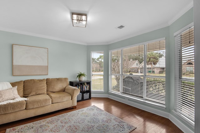 living area with ornamental molding, wood-type flooring, visible vents, and baseboards