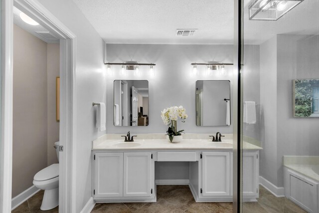 bathroom with double vanity, visible vents, toilet, a textured ceiling, and a sink