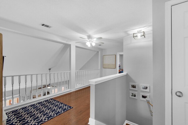 hallway with an upstairs landing, wood finished floors, and visible vents