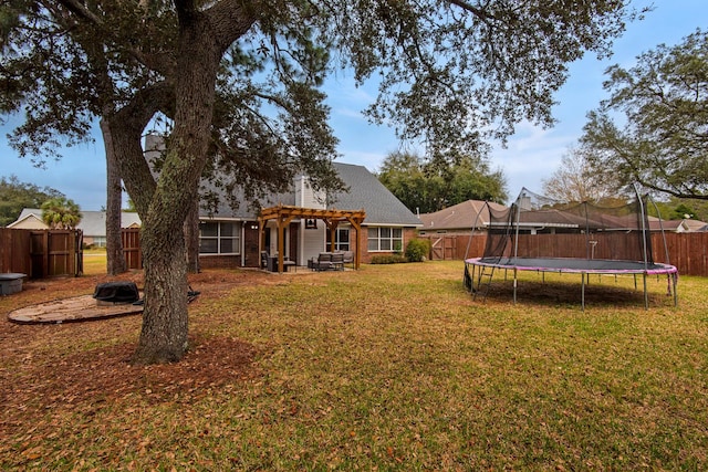 back of house featuring a fenced backyard, brick siding, a yard, a pergola, and a trampoline