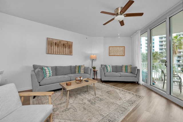 living area with a ceiling fan, a wall of windows, baseboards, and wood finished floors