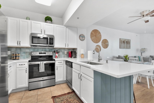 kitchen featuring a peninsula, a sink, open floor plan, appliances with stainless steel finishes, and tasteful backsplash