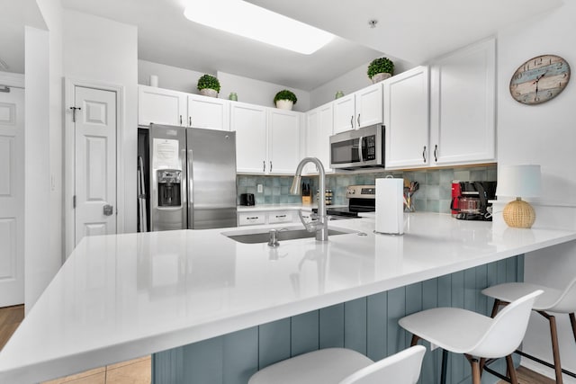 kitchen featuring stainless steel appliances, backsplash, white cabinets, a sink, and a peninsula