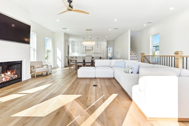 living room with ceiling fan, recessed lighting, stairway, light wood-type flooring, and a glass covered fireplace