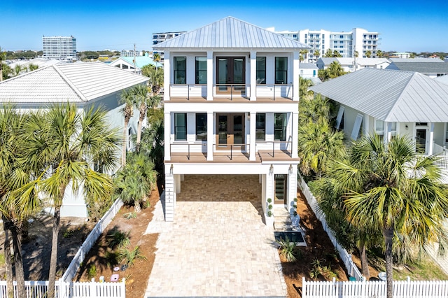 rear view of property featuring decorative driveway, french doors, fence, a balcony, and metal roof