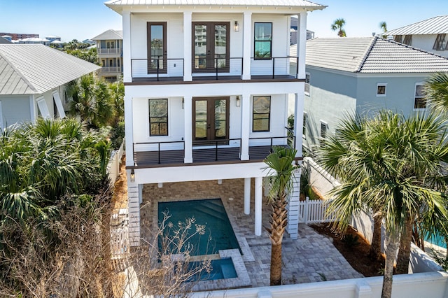 back of property with a balcony, metal roof, fence, french doors, and stucco siding