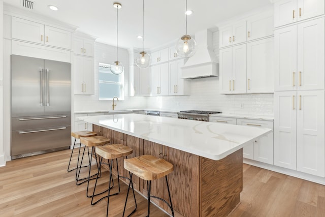 kitchen with white cabinets, stainless steel appliances, light wood-style flooring, and custom range hood