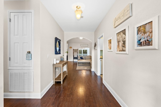 hallway with arched walkways, dark wood-style floors, visible vents, and baseboards