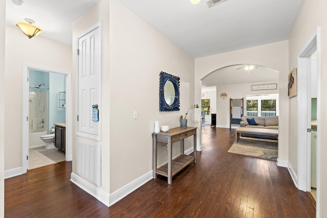 corridor featuring arched walkways, visible vents, hardwood / wood-style flooring, and baseboards