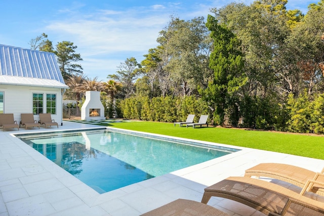 pool featuring a warm lit fireplace, a patio area, and a yard