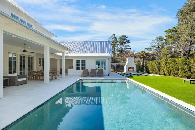 pool featuring a ceiling fan, a patio area, a yard, and a lit fireplace