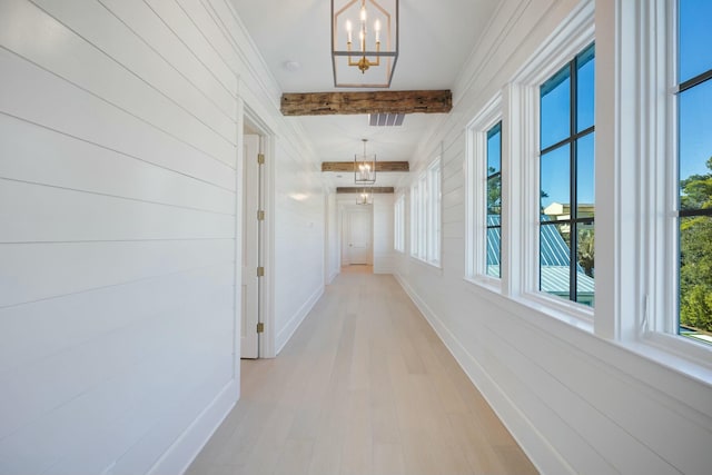 hallway featuring baseboards, light wood finished floors, beam ceiling, and a notable chandelier