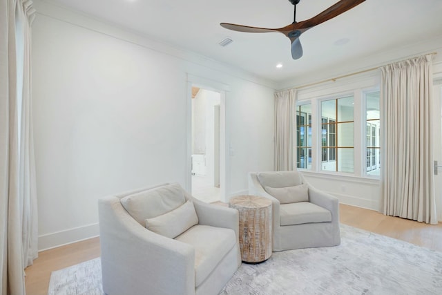 living area with light wood finished floors, baseboards, visible vents, a ceiling fan, and ornamental molding