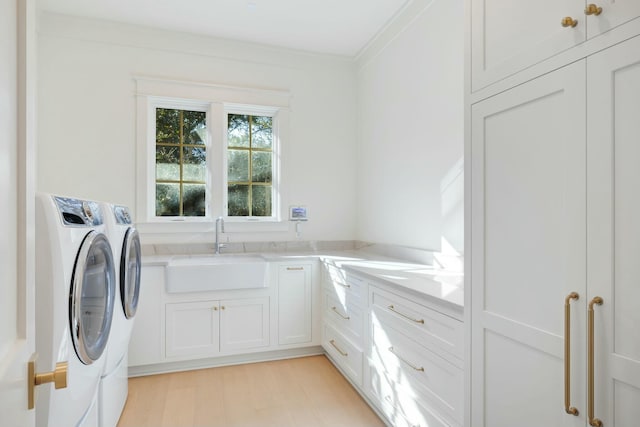 laundry room with cabinet space, ornamental molding, light wood-style floors, washing machine and dryer, and a sink