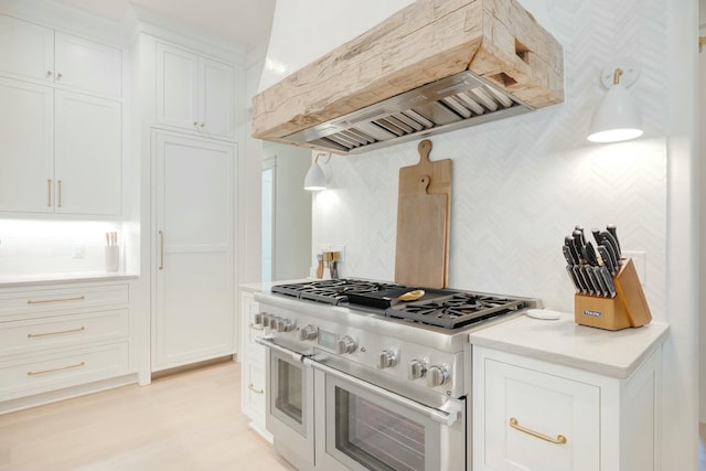 kitchen featuring range with two ovens, white cabinets, light countertops, custom exhaust hood, and decorative backsplash