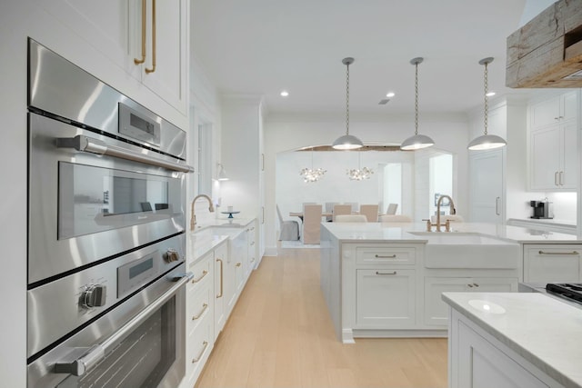 kitchen with light wood-type flooring, stainless steel double oven, white cabinets, and a sink