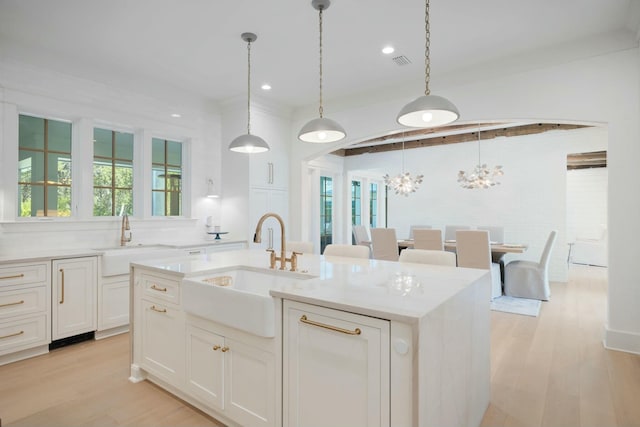 kitchen with light wood finished floors, a sink, visible vents, and white cabinets