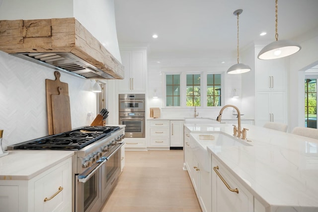 kitchen featuring appliances with stainless steel finishes, a kitchen island with sink, premium range hood, white cabinetry, and backsplash