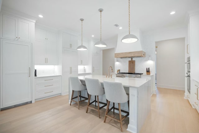 kitchen featuring light wood-style flooring, decorative backsplash, white cabinets, an island with sink, and a kitchen breakfast bar