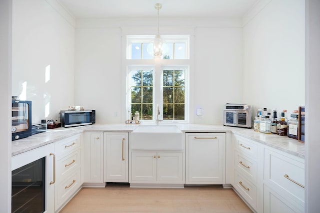 kitchen featuring crown molding, stainless steel microwave, white cabinetry, a sink, and beverage cooler