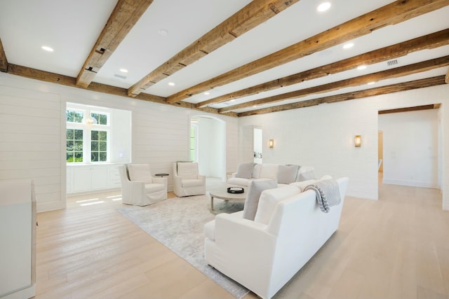 living room featuring arched walkways, beam ceiling, and light wood-style floors