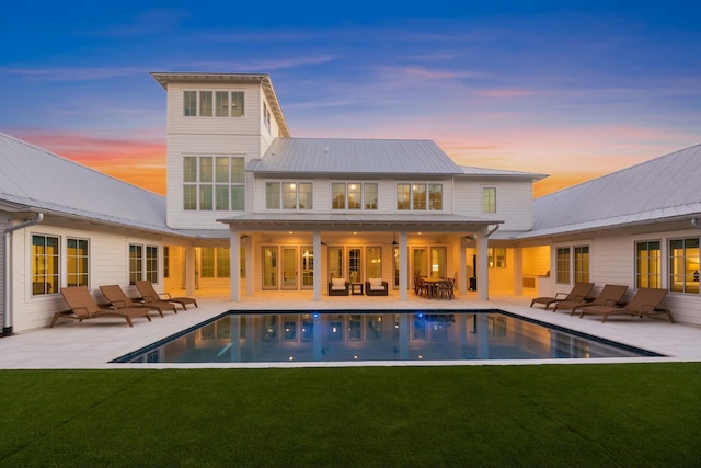 rear view of property featuring a patio area, an outdoor pool, and a lawn