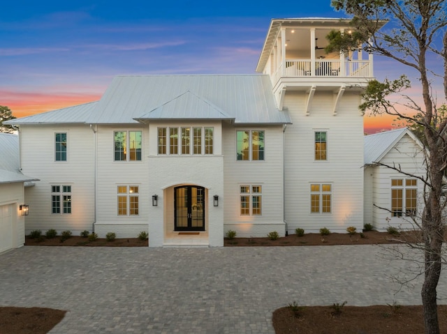 view of front of house with a balcony, brick siding, metal roof, and french doors